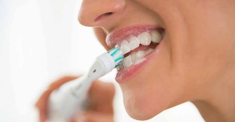 Woman brushing teeth with electric toothbrush.