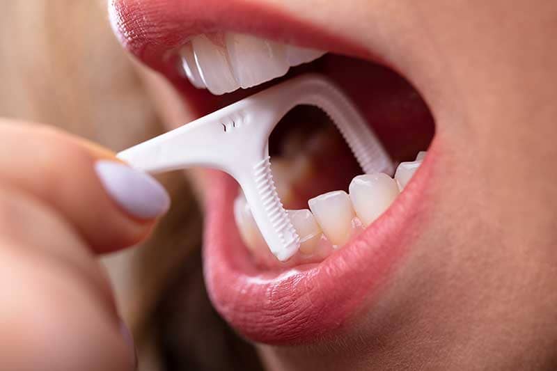Woman using a dental pick to clean teeth.